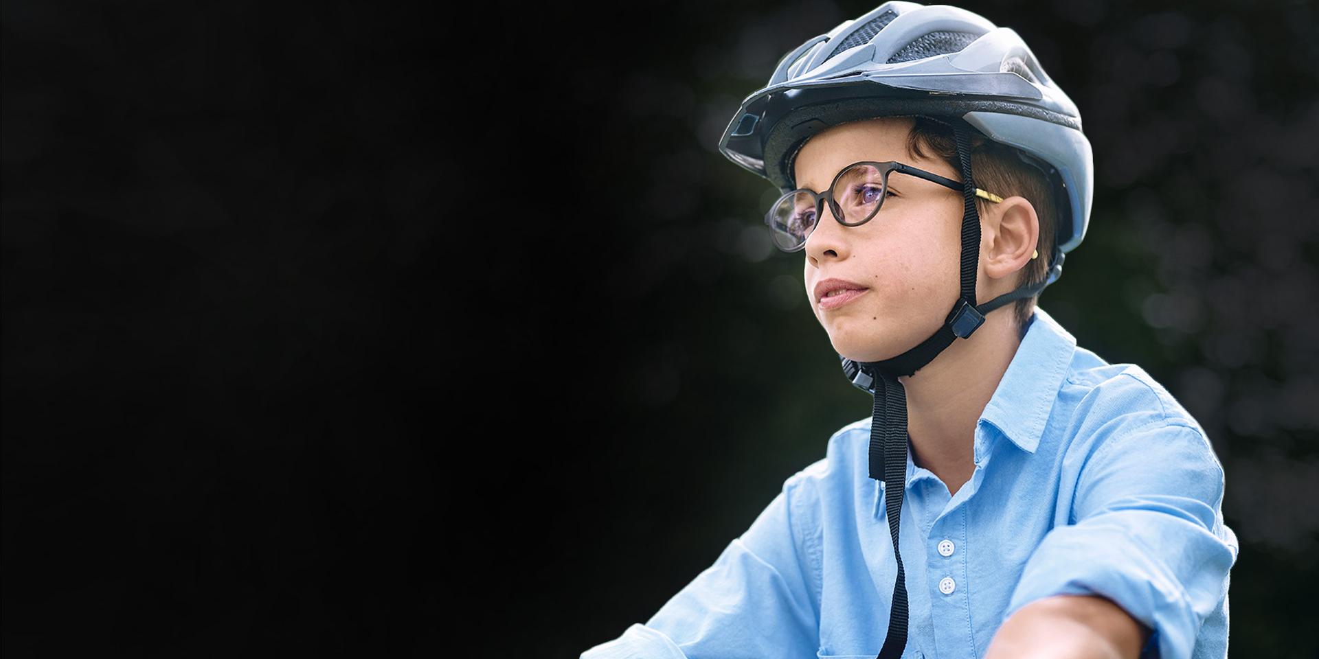 Gözlüklü ve kasklı genç bir çocuk bisiklet sürerken görülüyor.