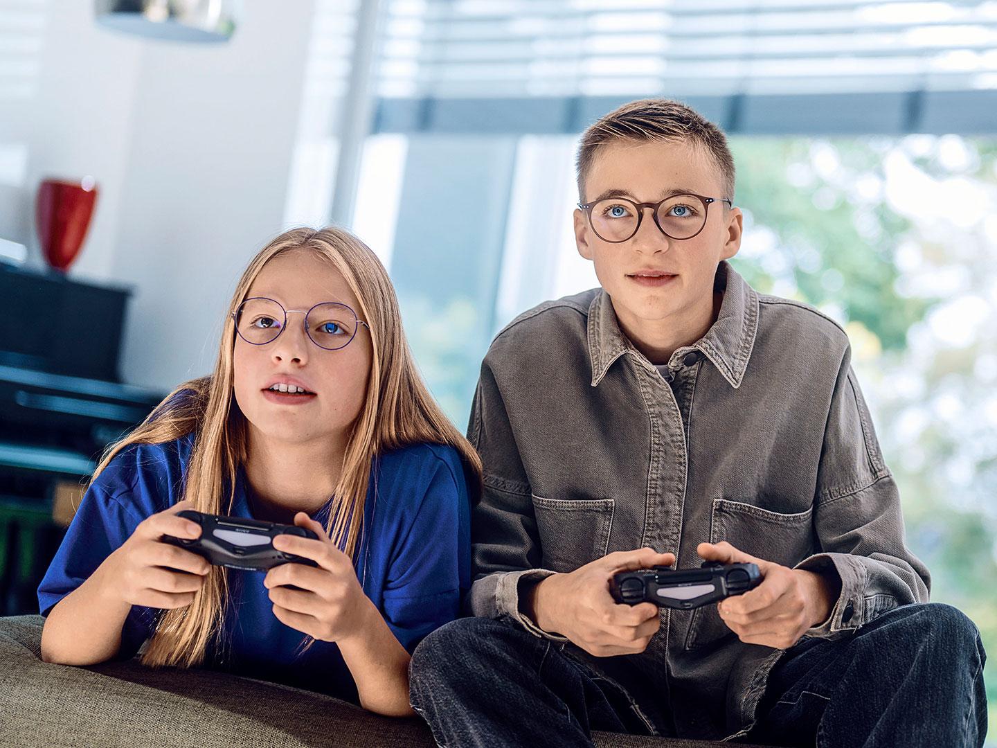 Konsolda video oyunları oynayan genç bir kız ve erkek.