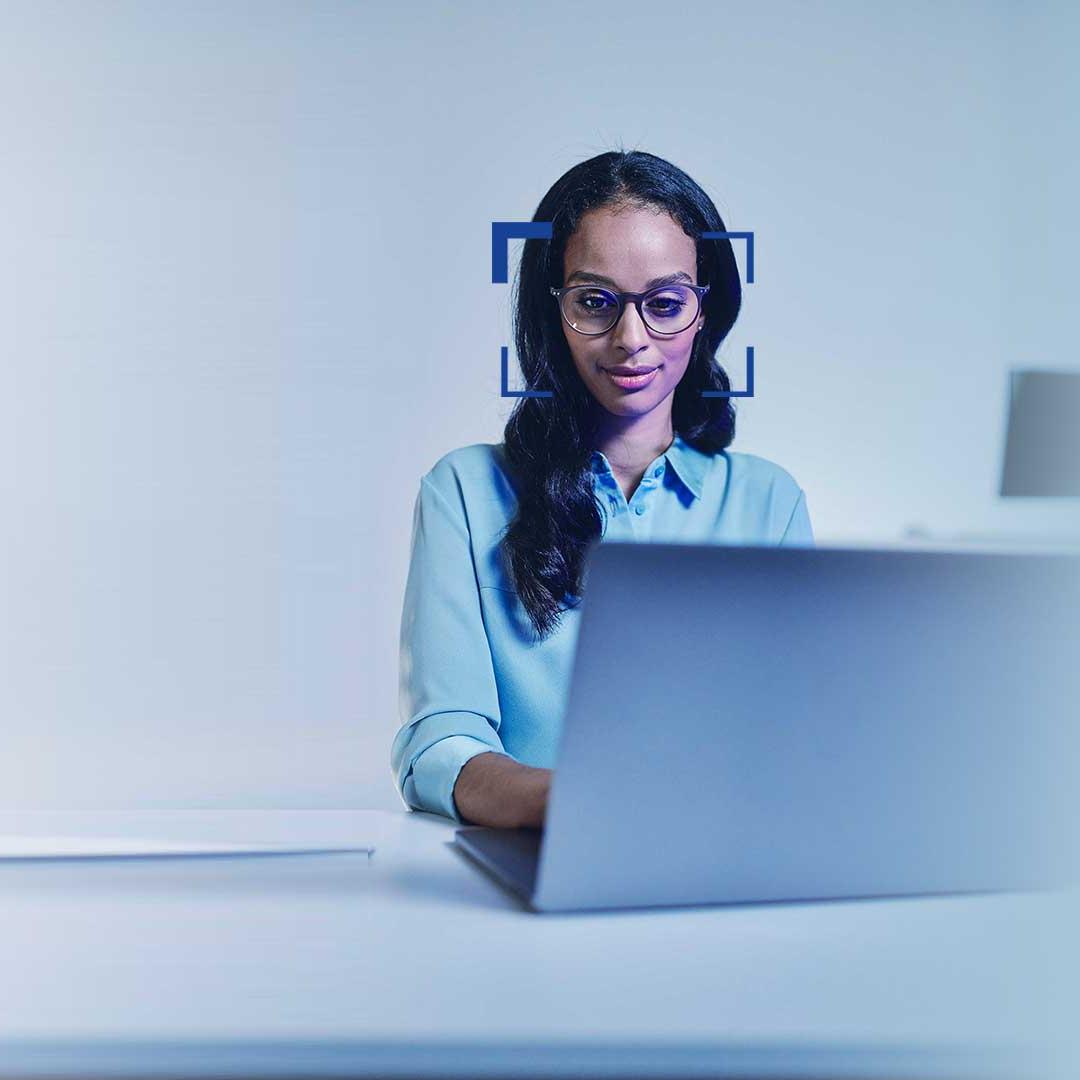 Siyah saçlı ve gözlüklü bir kadın dizüstü bilgisayara gülümseyerek bakıyor.