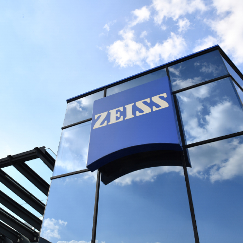Üzerinde büyük bir ZEISS logosu bulunan modern bir cam binanın görüntüsü. 
