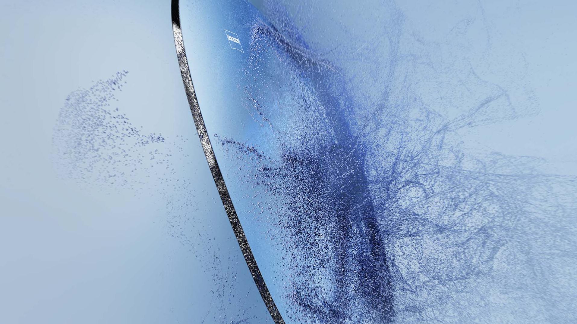 ZEISS logolu bir gözlük camı kumla çarpışıyor.