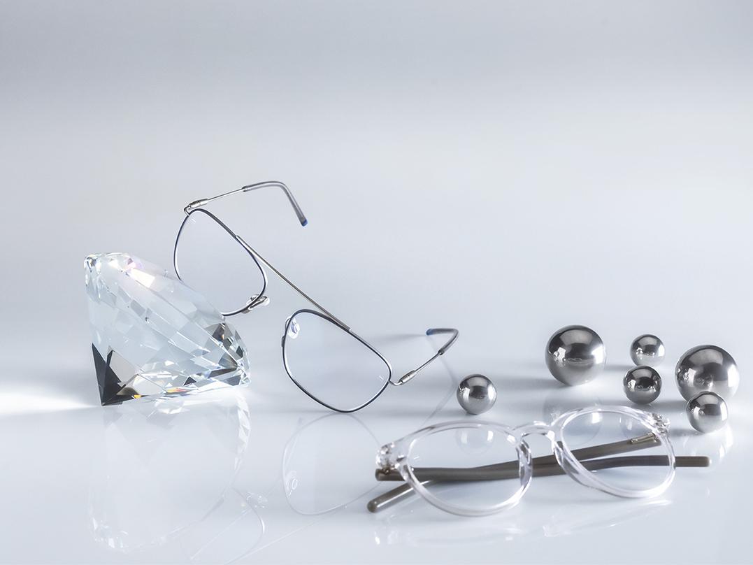 ZEISS camları DuraVision® AntiVirus Platinum kaplama ile kaplanmış, en sert ve en hijyenik iki gözlük. Bir bardak kristalin önünde duruyor, diğeri gümüşün yanında, yerde yatıyor. Her ikisinin de mavimsi yansımalar içermeyen şeffaf camları var. 
