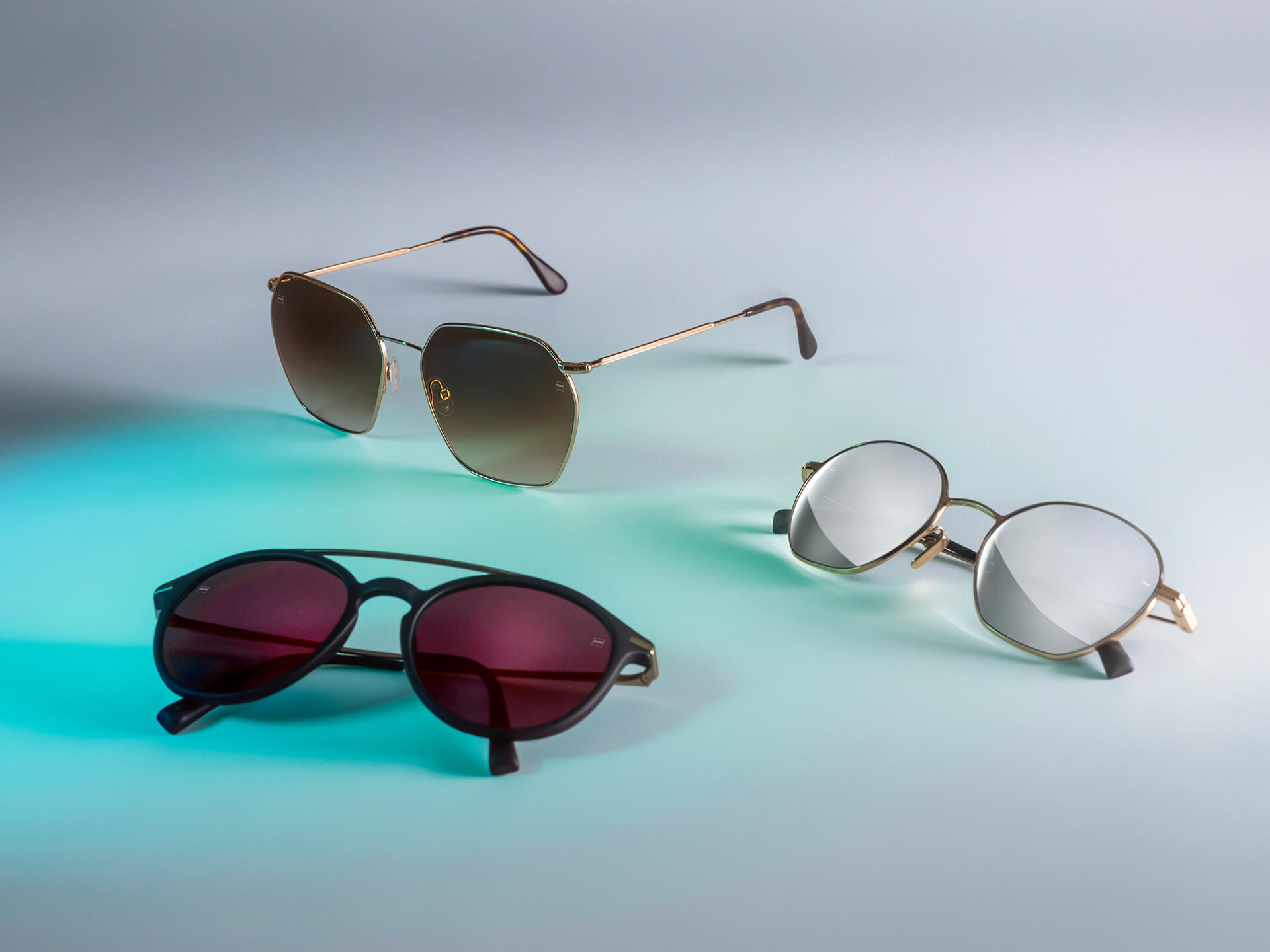 Beyaz bir arka planda mavi ışık yansımasıyla görülebilen, DuraVision Sun, DuraVision Mirror ve Flash Mirror kaplamalı, farklı renklerde ZEISS güneş gözlüğü camlarına sahip üç çift güneş gözlüğü.