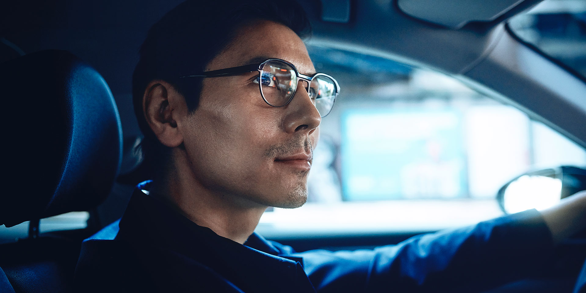 Yolda hafif bir gülümsemeyle kendine güvenen bir şekilde araba kullanan adam. ZEISS DriveSafe tek odaklı gözlük camları kullanıyor.