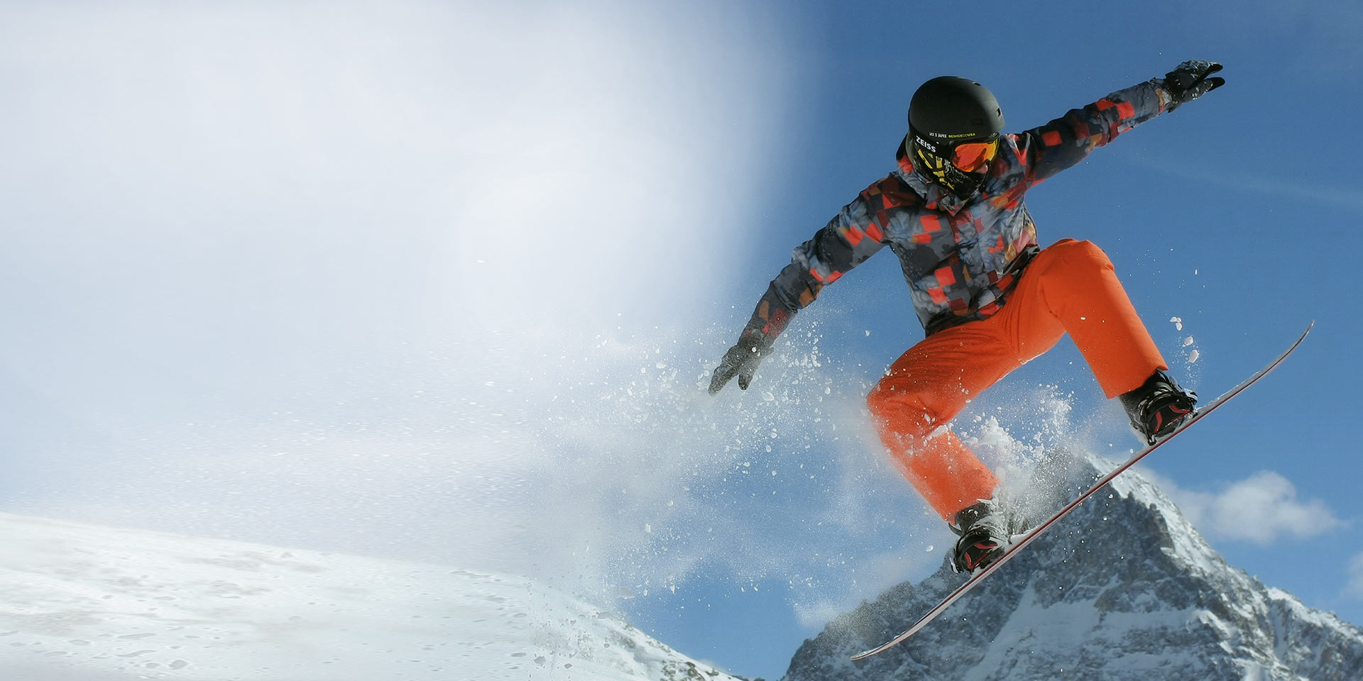 Bir adam snowboard ile atlıyor, siyah bir kayak kaskı ve koruma için Değiştirilebilir teknolojiye sahip ZEISS kar gözlüğü takıyor