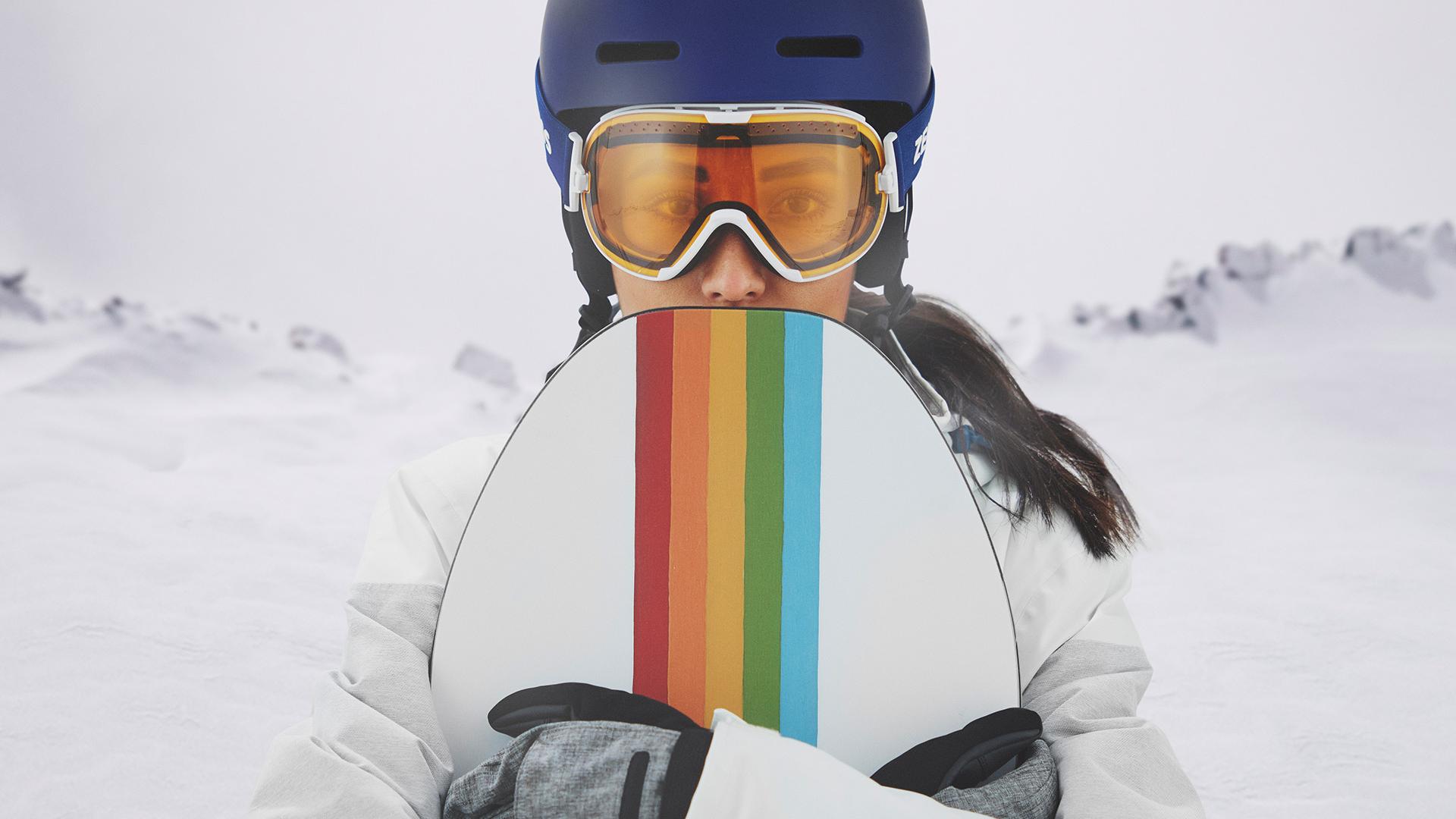 ZEISS Interchangeable teknolojisine sahip kar gözlüğü takan ve bir snowboard tutan genç bir kadın.