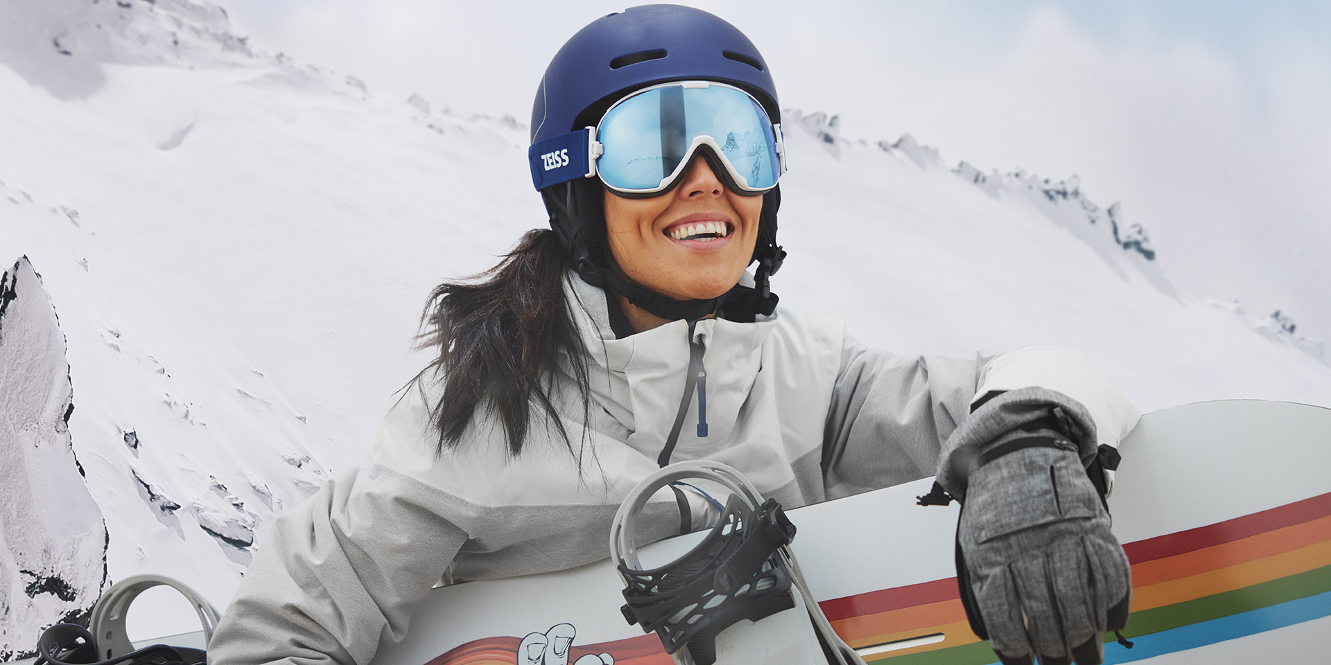 ZEISS Interchangeable teknolojisine sahip kar gözlüğü takan ve bir snowboard tutan genç bir kadın.
