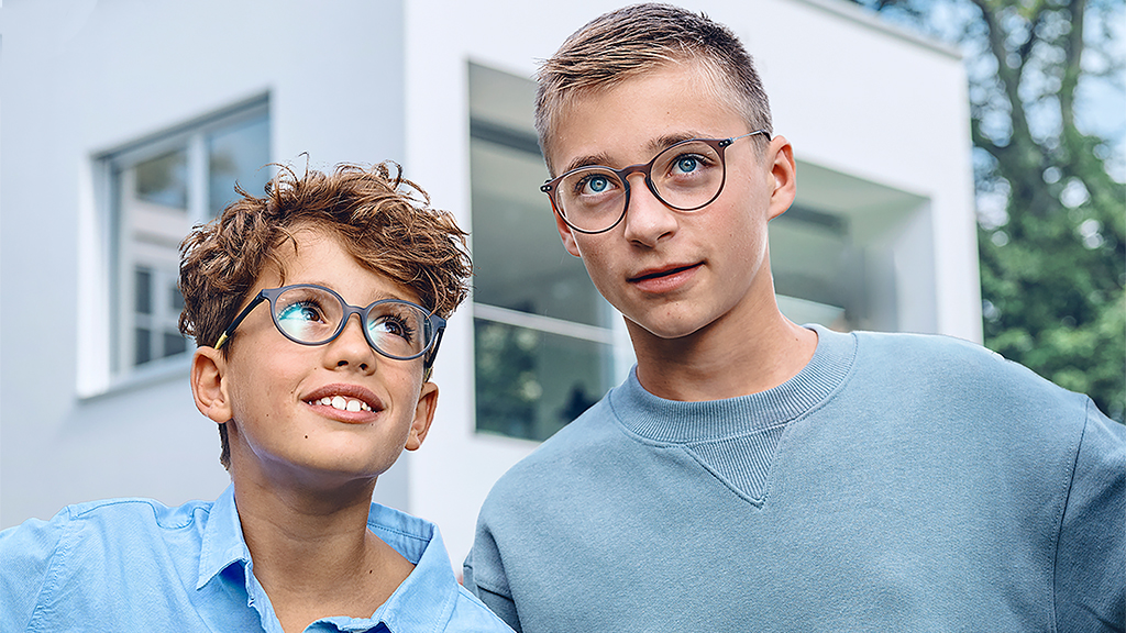 Genç bir çocuk, her ikisi de ZEISS Single Vision SmartLife Young gözlükleri takan bir genç çocuğa bakıyor